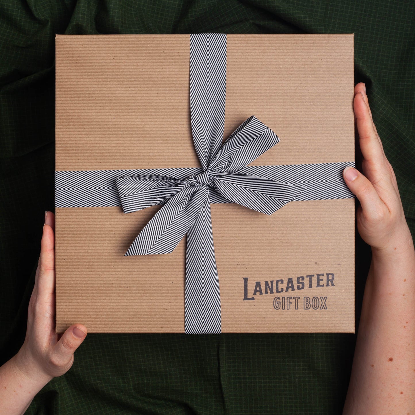 Hands holding a Lancaster Gift Box with black & white bow.